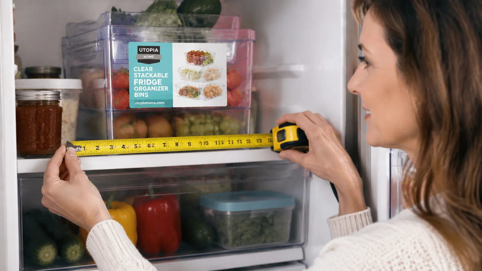 Person measuring refrigerator shelf depth with a tape measure before buying organizer bins